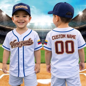May include: A white baseball jersey with blue trim and the word "Venezuela" in brown script. The jersey has a button-up front and is paired with a navy blue baseball cap. The back of the jersey has "CUSTOM NAME" and the number "00".