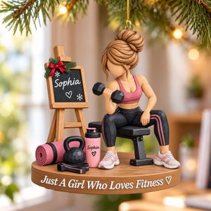 Könnte beinhalten: Ein dekoratives Ornament mit einer skulptierten Figur mit braunem Dutt, die ein pinkes Sport-Top und eine schwarze Leggings trägt und eine schwarze Hantel auf einer Bank hebt. Enthält eine pinke Trinkflasche mit der Aufschrift Sophia, eine Yogamatte und eine Staffelei mit dem Namen Sophia. Der Sockel trägt den Text Just A Girl Who Loves Fitness.