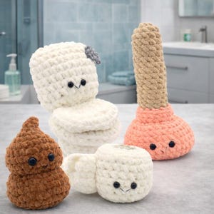 Puede incluir: Cuatro peluches de ganchillo con temática de baño. Un inodoro blanco con tapa gris, un emoji de caca marrón, un rollo de papel higiénico y un desatascador rosa y beige, todos con caras sonrientes y ojos de botón negros.