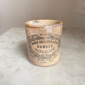 May include: An antique Dundee Marmalade jar. The off-white ceramic jar features black text and a decorative border. The text reads "JAMES KEILLER & SONS DUNDEE MARMALADE" and "PRIZE MEDAL FOR MARMALADE LONDON. 1862".