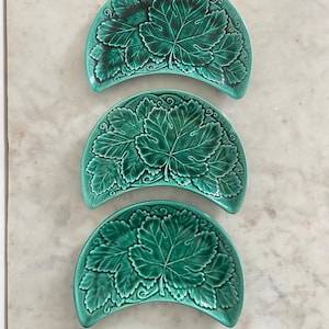 May include: Three crescent-shaped ceramic dishes in a vibrant green glaze. Each dish features a detailed, embossed relief pattern of grape leaves and vines covering the entire surface, with darker green shading highlighting the leaf veins.