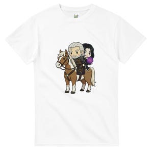 May include: White t-shirt featuring a cartoon illustration of two characters riding a brown and white horse. The characters have white and black hair, and the woman is holding a purple orb. The shirt has a small logo near the neckline.