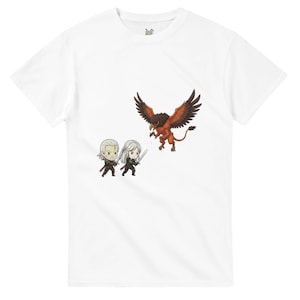 May include: White t-shirt featuring a cartoon illustration of two figures with swords facing a red and brown griffin. The figures have white hair and are dressed in black. The griffin has outstretched wings.