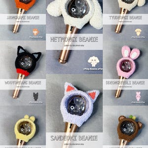 Può includere: Una collezione di coperture per light stick all'uncinetto fatte a mano in vari design di animali, tra cui un orso, un gatto e un coniglio. Ogni copertura ha una combinazione di colori unica ed è progettata per adattarsi a un modello specifico di light stick. Il testo "JJONGRAMI BEANIE" è visibile.