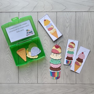 May include: A green plastic container with ice cream cone and scoop cutouts, and task cards. The task cards feature ice cream cones with various flavours and a cherry on top. The text on the card reads "Create your ice cream cone/bowl to match each task card."