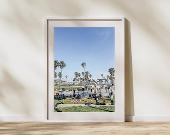 Peut inclure: Photographie encadrée d'une journée ensoleillée dans un parc avec des palmiers. Des personnes sont rassemblées sur l'herbe et les allées. Le ciel est bleu clair. Le cadre est blanc et le sol est en bois.