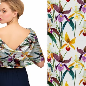 Könnte beinhalten: Ein weißer Schal mit einem Blumendruck von Orchideen in den Farben Lila, Gelb und Rot. Der Schal ist über die Schultern einer Person gelegt.