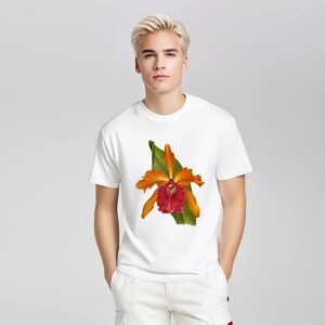 May include: White t-shirt featuring a vibrant orange and red orchid flower design with green leaves. The short-sleeved tee is worn by a person with blonde hair and white pants. The orchid design is centered on the shirt.