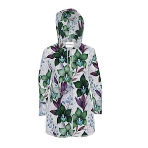 Puede incluir: Vestido con capucha y mangas largas con estampado floral. El diseño presenta grandes orquídeas verdes, hojas moradas y pequeñas bayas azules sobre un fondo blanco. Tiene un cordón en el cuello y una capucha.