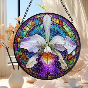 May include: A round stained glass window featuring a white and purple orchid with a colorful mosaic background. The orchid has detailed petals and a vibrant center. The window is framed in black and hangs from a chain.