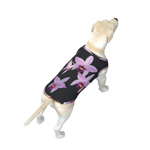May include: A white dog wearing a black sleeveless tank top with a pink orchid floral print.