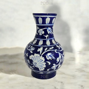 Può includere: Un vaso in ceramica blu cobalto con motivi floreali bianchi. Il vaso ha un corpo bulboso, un collo stretto e un bordo svasato. Il design floreale comprende fiori e foglie stilizzate. La base del vaso ha il testo "POC".