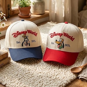 May include: Two baseball caps with the text "Disney World" in red script. One cap has a blue brim and features Goofy, the other has a red brim and features Pluto. Both caps have "Est. 1971."