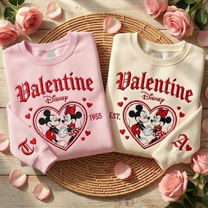 Puede incluir: Dos sudaderas de San Valent&iacute;n, una rosa y otra crema, con Mickey y Minnie Mouse en un dise&ntilde;o en forma de coraz&oacute;n. La palabra "Valentine" est&aacute; bordada en escritura roja sobre el logotipo de Disney. Las mangas tienen las letras "T" y "A".