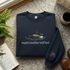 May include: Navy blue sweatshirt featuring a loon graphic and the text "stupid canadian wolf bird." The sweatshirt also has embroidered hockey sticks and the numbers "24" and "81" on the sleeve.
