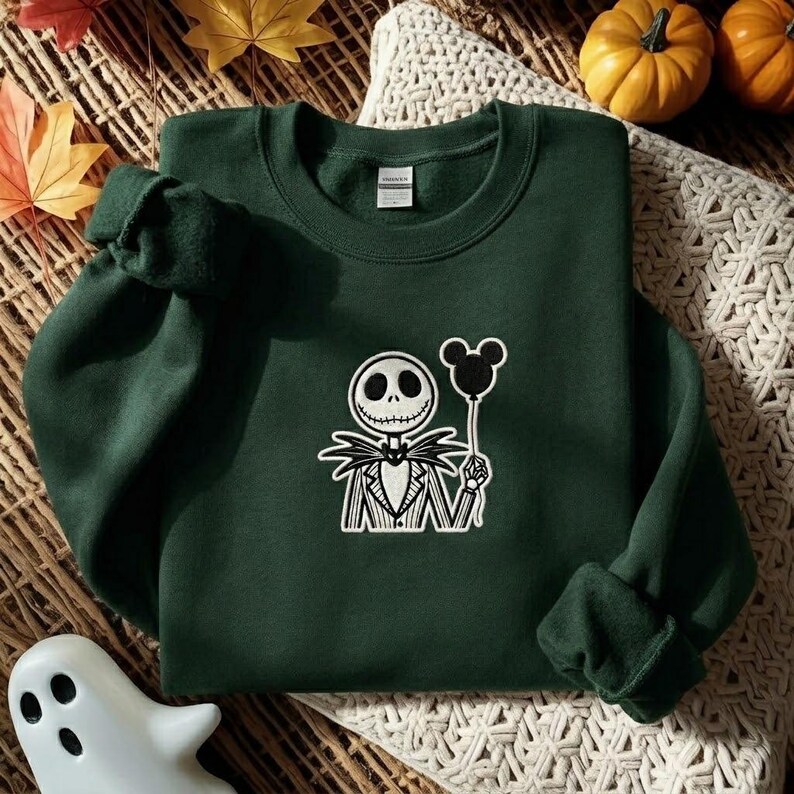 May include: A dark green crewneck sweatshirt featuring a white embroidered graphic of a skeletal character in a pinstriped suit holding a black balloon shaped like a mouse head. The garment has long sleeves, a ribbed neckline, and a white brand label.