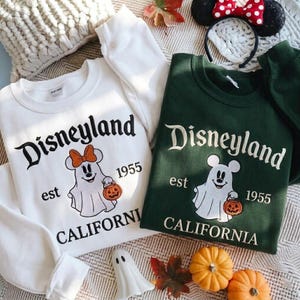 May include: A white sweatshirt and a dark green sweatshirt, both featuring embroidered text reading Disneyland est 1955 California and a graphic of a ghost wearing mouse ears and holding a jack-o'-lantern pumpkin bucket.