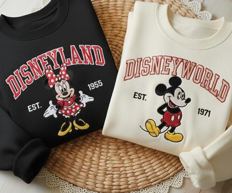 May include: Black sweatshirt with "Disneyland" in red arched text, featuring Minnie Mouse. A cream-colored sweatshirt displays "Disneyworld" with Mickey Mouse. Both sweatshirts have the establishment years 1955 and 1971.