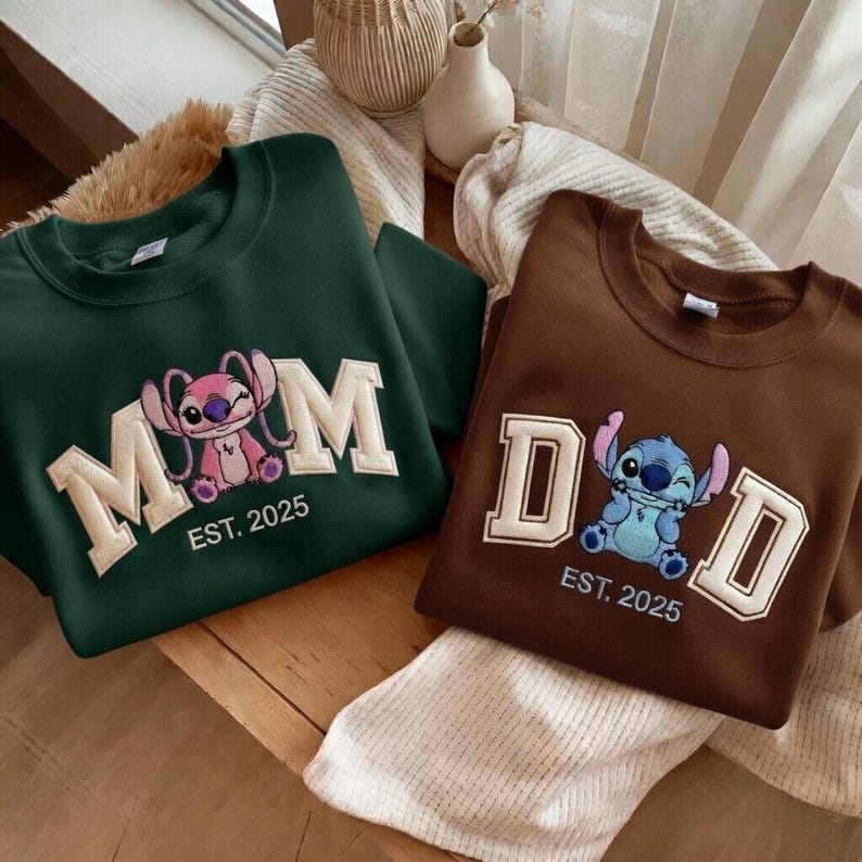 Puede incluir: Dos sudaderas, una verde oscuro y otra marr&oacute;n. La verde tiene "MOM" con un personaje de dibujos animados rosa y "EST. 2025". La marr&oacute;n tiene "DAD" con un personaje azul y "EST. 2025".
