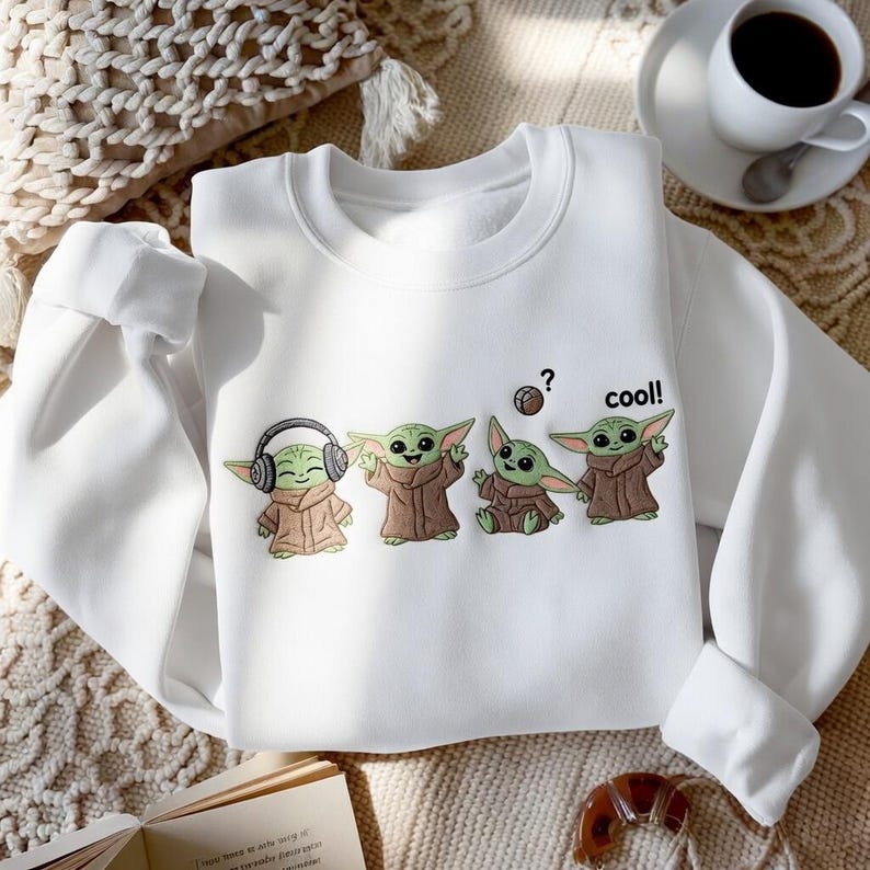 May include: White sweatshirt featuring a graphic of four Grogu characters in various poses. One Grogu wears headphones, another has arms raised, and a third is seated. The word "cool!" is printed next to the last Grogu.