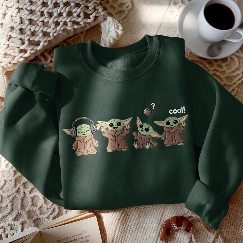 May include: Dark green sweatshirt featuring a graphic of four cartoon characters. The characters are green with large ears and brown robes. One character wears headphones, and another has a question mark above its head. The word "cool!" is printed on the sweatshirt.