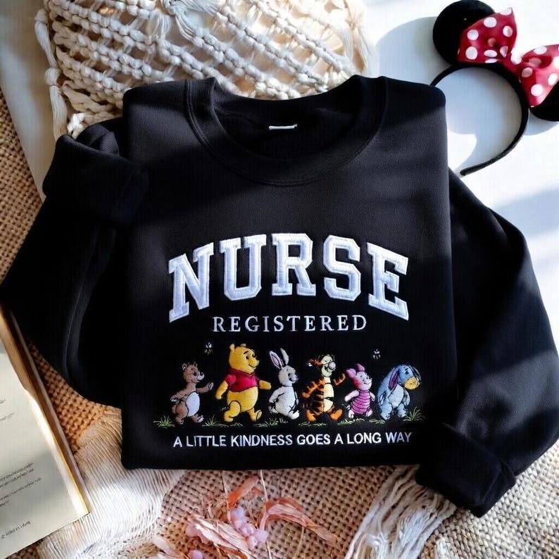 May include: Black sweatshirt with the word "NURSE" in white block letters above "REGISTERED". Below, cartoon characters walk across the bottom. The phrase "A LITTLE KINDNESS GOES A LONG WAY" is printed below the characters.