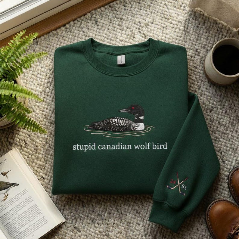 May include: A dark green sweatshirt with a graphic of a loon bird on water and the text "stupid canadian wolf bird". The sleeve has an embroidered design of crossed hockey sticks and the numbers 24 and 81.