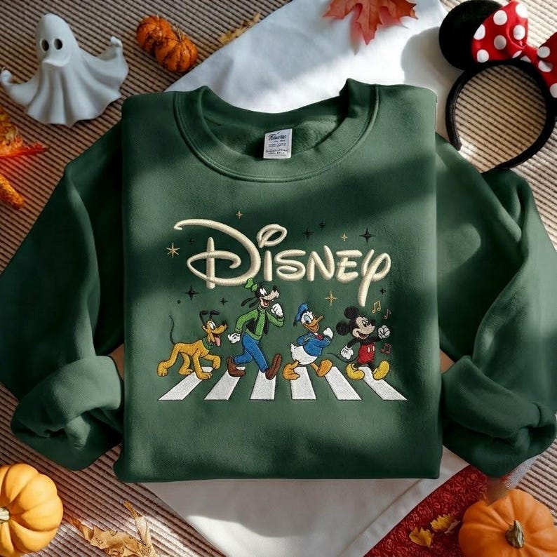 Peut inclure: Un sweat-shirt &agrave; col rond vert fonc&eacute; avec une broderie repr&eacute;sentant Pluto, Dingo, Donald et Mickey marchant sur un passage pi&eacute;ton blanc. Le mot Disney est brod&eacute; en lettres cursives cr&egrave;me au-dessus des personnages avec de petites &eacute;toiles.