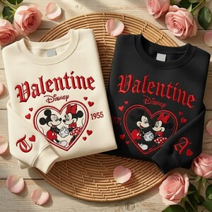 Puede incluir: Dos sudaderas, una crema y otra negra, con un dise&ntilde;o de San Valent&iacute;n. El dise&ntilde;o incluye la palabra "Valentine" en rojo, el logo de Disney y un coraz&oacute;n con Mickey y Minnie Mouse. El a&ntilde;o "1955" tambi&eacute;n est&aacute; presente.