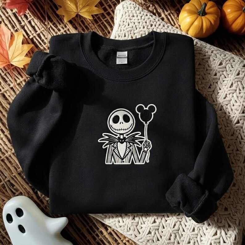 May include: A black long-sleeve sweatshirt featuring a white graphic of a skeletal character wearing a pinstriped suit and bowtie, holding a balloon shaped like a mouse head. The garment has a crew neckline and ribbed cuffs at the sleeves.
