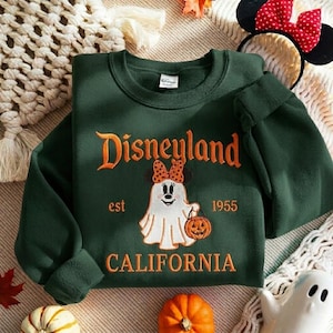 May include: A dark green crewneck sweatshirt featuring an embroidered graphic of a ghost wearing a polka dot bow and holding a pumpkin. The text reads Disneyland est 1955 CALIFORNIA in orange lettering. The garment has long sleeves and a ribbed collar.