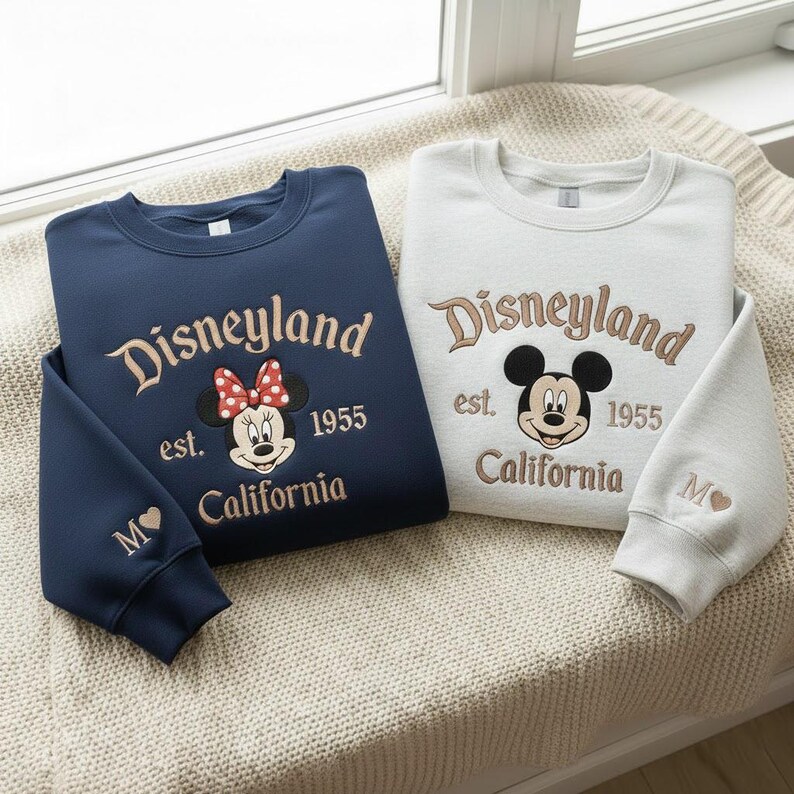 Puede incluir: Dos sudaderas con el logo de Disneyland, est. 1955, y "California" bordado en color beige. Una es azul marino con un dise&ntilde;o de Minnie Mouse, la otra es gris claro con un dise&ntilde;o de Mickey Mouse. Ambas tienen una inicial bordada en la manga.
