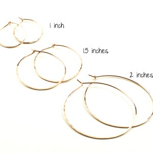 May include: Rose gold hoop earrings in three sizes: 1 inch, 1.5 inches, and 2 inches. The earrings are displayed on a white background. The text "1 inch", "1.5 inches", and "2 inches" is written above the corresponding earrings.