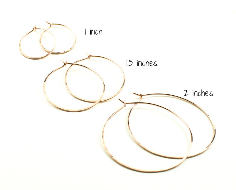 May include: Rose gold hoop earrings in three sizes: 1 inch, 1.5 inches, and 2 inches. The earrings are displayed on a white background. The text "1 inch", "1.5 inches", and "2 inches" is written above the corresponding earrings.