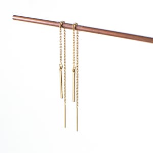 May include: A pair of gold chain earrings with a small gold bar hanging from each chain.