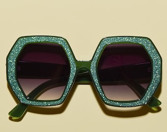 May include: Green octagon-shaped sunglasses with glitter accents and dark lenses.