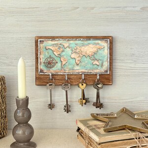 May include: A wooden key holder with a world map design in shades of blue and brown. The key holder has four metal hooks with vintage keys hanging from them. A compass rose is in the upper left corner.