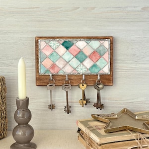 Könnte beinhalten: Ein hölzerner Schlüsselhalter mit einem Buntglasdesign in Rosa, Türkis und Weiß. Der Schlüsselhalter hat vier Metallhaken mit antiken Schlüsseln. Ein Kerzenhalter und eine sternförmige Schale sind ebenfalls zu sehen.