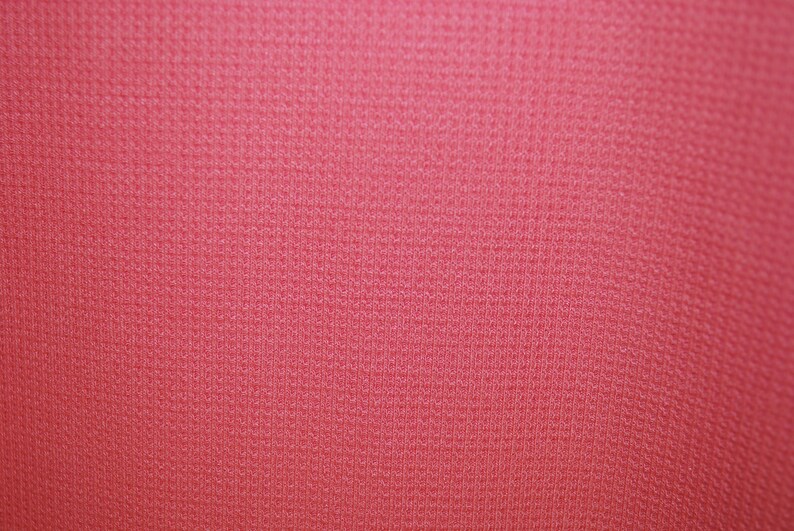 May include: A close-up of a textured, pink fabric. The fabric has a subtle sheen and a fine weave.