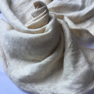 Peut inclure: Tissu cr&egrave;me, finement tiss&eacute;, d'aspect doux et textur&eacute;. Le tissu est drap&eacute; et pli&eacute;, cr&eacute;ant un motif tourbillonnant. Les bords du tissu sont l&eacute;g&egrave;rement effiloch&eacute;s. L'aspect g&eacute;n&eacute;ral est naturel et organique.