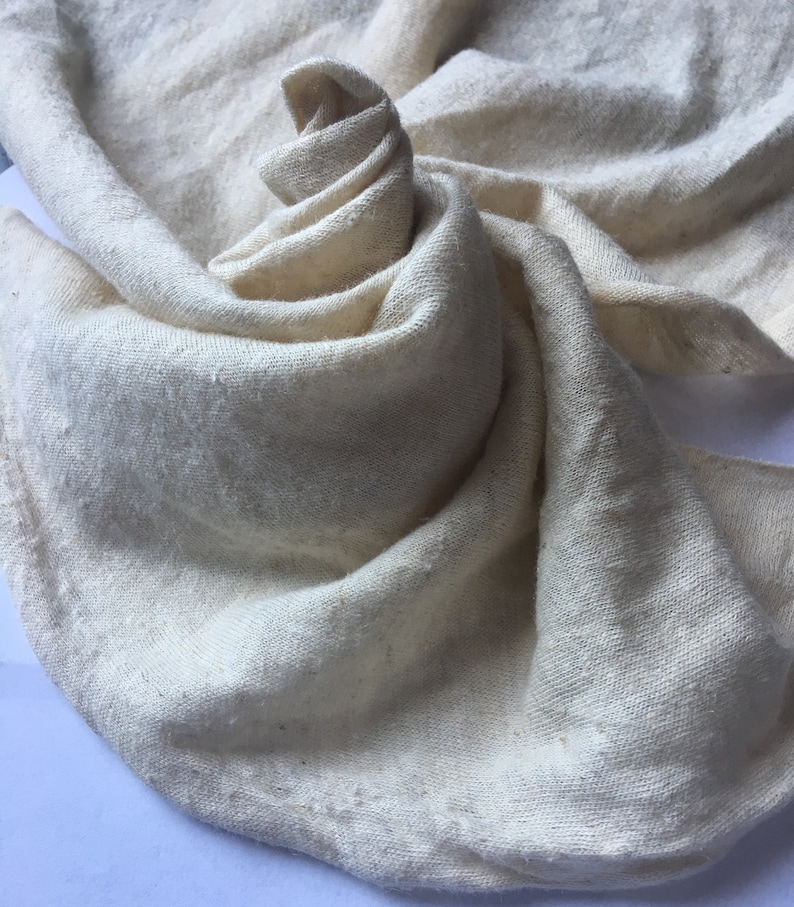 Peut inclure: Tissu cr&egrave;me, finement tiss&eacute;, d'aspect doux et textur&eacute;. Le tissu est drap&eacute; et pli&eacute;, cr&eacute;ant un motif tourbillonnant. Les bords du tissu sont l&eacute;g&egrave;rement effiloch&eacute;s. L'aspect g&eacute;n&eacute;ral est naturel et organique.
