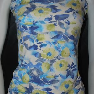 May include: White fabric with a blue and green floral print. The fabric has a watercolor effect and features a variety of flower shapes and sizes.