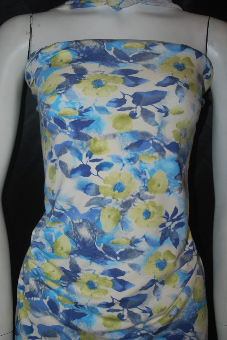 May include: White fabric with a blue and green floral print. The fabric has a watercolor effect and features a variety of flower shapes and sizes.