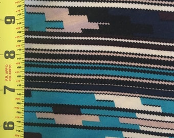May include: A close-up of a turquoise, black, white, and gray patterned fabric. The fabric has a striped pattern with geometric shapes.