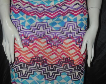 May include: A white fabric with a colorful geometric pattern. The pattern features a mix of pink, blue, orange, and purple colors. The fabric is textured and has a slight sheen.