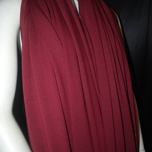 May include: A deep burgundy colored fabric with a smooth, slightly textured surface. The fabric is draped over a white mannequin.
