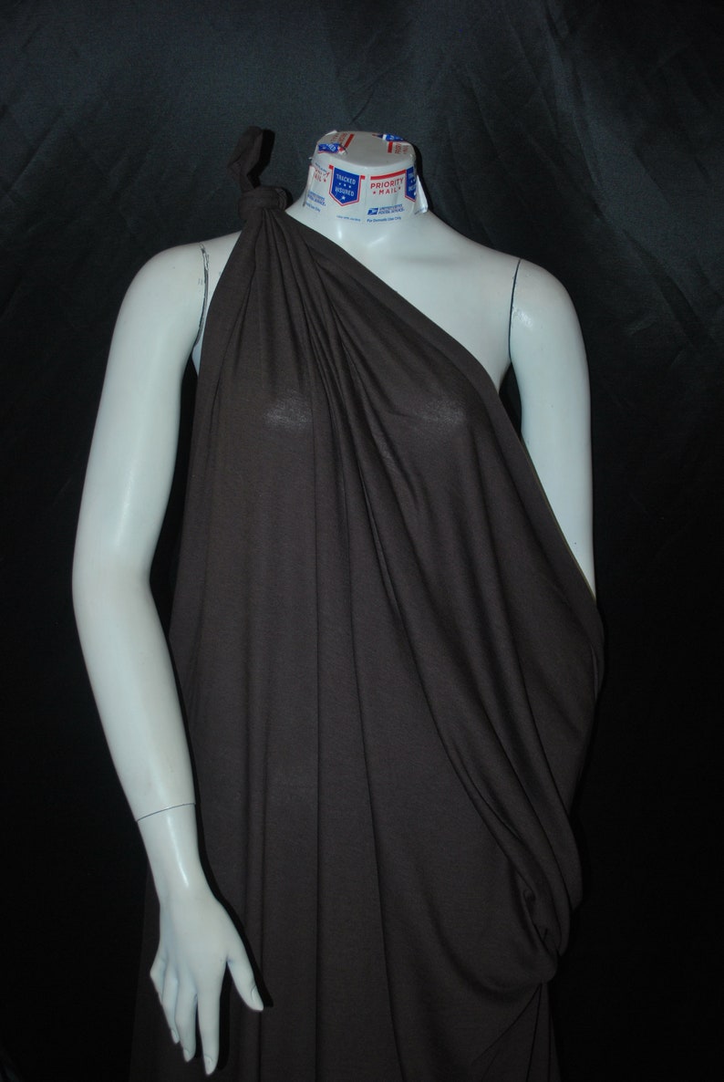 May include: A brown one-shoulder draped top made of a soft, flowing fabric. The top is draped over a white mannequin.