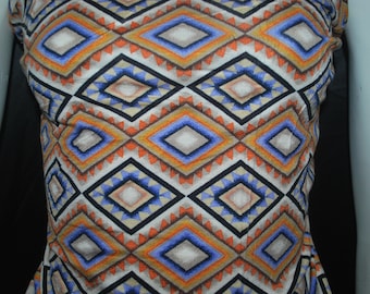 May include: A white fabric with a geometric pattern in shades of blue, orange, and brown. The pattern is made up of repeating diamonds and triangles.