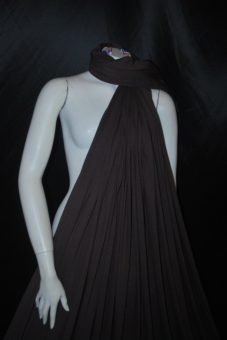 May include: A brown, drapey fabric scarf is draped over a white mannequin. The scarf is made of a soft, lightweight material and has a flowing, elegant look.