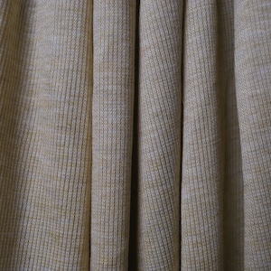 Puede incluir: Primer plano de una tela de punto de canal&eacute; beige con una textura sutil. La tela est&aacute; doblada de forma que crea l&iacute;neas verticales.